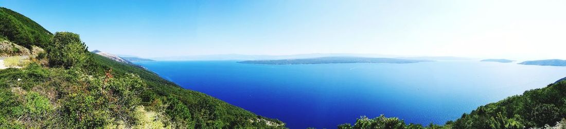 Scenic view of sea and mountains against clear blue sky