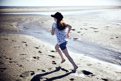 Playful girl running at beach on sunny day