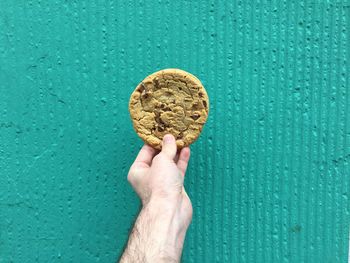 Cropped image of hand holding cookie against wall