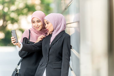 Portrait of woman holding mobile phone standing outdoors