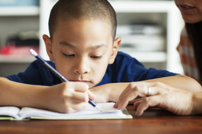 Cropped image of mother assisting son in studying at home reading book on bed at home