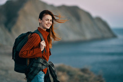 Portrait of smiling young woman standing against sea