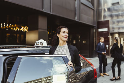 Smiling female entrepreneur looking away while entering in taxi