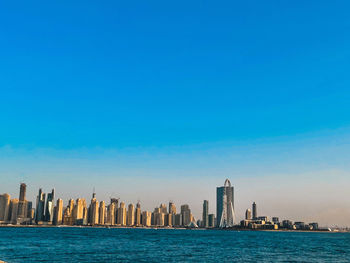 Sea by modern buildings in city against sky