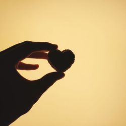 Close-up of hand holding heart shape against sky during sunset