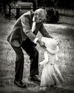 Senior man putting hat on granddaughter standing outdoors