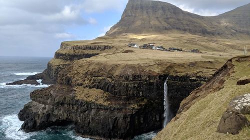 Scenic view of cliffs, a waterfall, and a village against sky