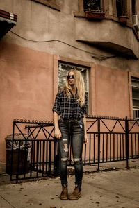 Full length of woman wearing sunglasses standing against building