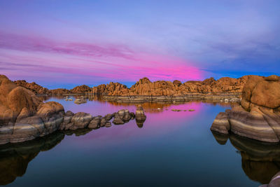 Rock formation by lake against sky during sunset