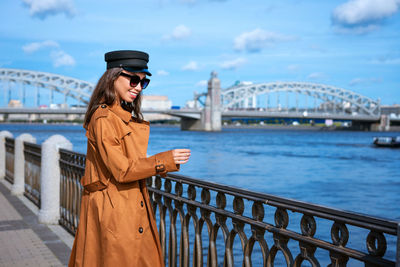 Happy young woman in light coat on the embankment posing