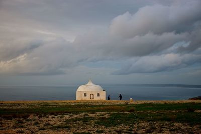 Built structure on field by sea against cloudy sky