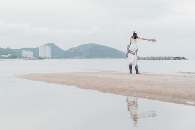 Rear view of woman standing at beach against sky