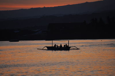 Silhouette people on boat sailing on sea against sky during sunset