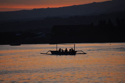 Silhouette people on boat sailing on sea against sky during sunset