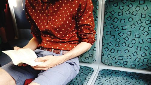 Midsection of man reading book while sitting in train