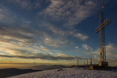 Cross on snowcapped mountain against sky during sunset