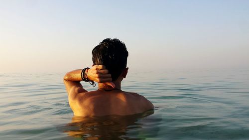 Rear view of shirtless woman standing in sea against sky