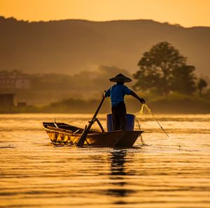 Silhouette man standing on boat against sky during sunset