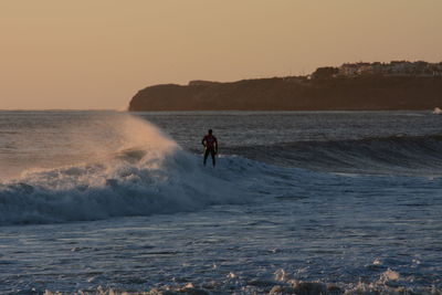 Man in sea against clear sky during sunset