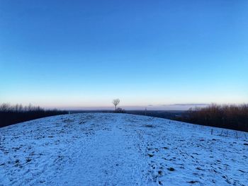 Snow covered field against clear blue sky