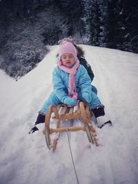 Cute siblings wearing warm clothing while sitting on sled in snow