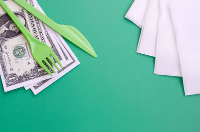 High angle view of cutleries with money and tissue papers on green background