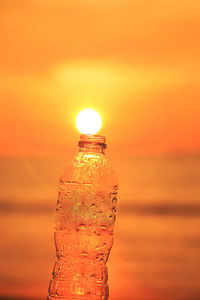 Close-up of water bottle against orange sky