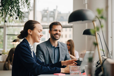 Male and female business colleagues discussing over laptop at desk in creative office