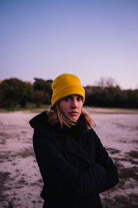 Portrait of young woman in hat standing against sky during winter