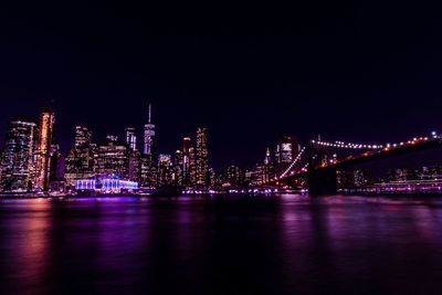 Illuminated bridge over river against buildings at night