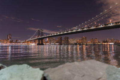 Illuminated bridge over river with city in background