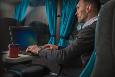 Side view of man using laptop in bus