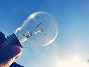 Cropped hand holding light bulb against sky