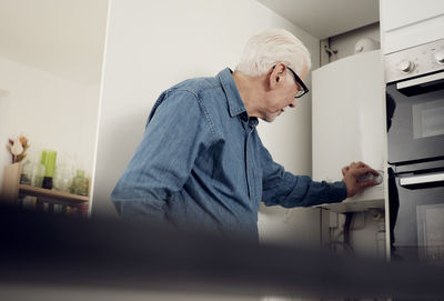 Senior man adjusting boiler for energy saving at home