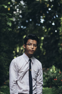 Portrait of young man standing against trees in park