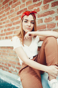 Portrait of woman sitting against brick wall