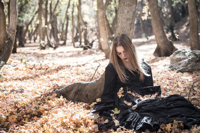 Depressed young woman sitting on dry leaves in forest