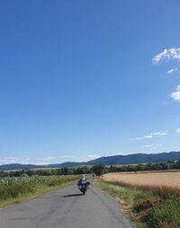 People riding motorcycle on road amidst field against sky