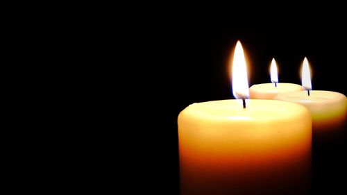 Close-up of burning candle against black background