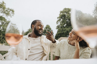 Smiling man gesturing while talking to female friend during dinner party at cafe