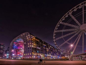 Low angle view of ferris wheel and illuminated market hall sky at night