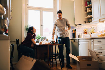 Smiling woman looking at man holding glass in kitchen