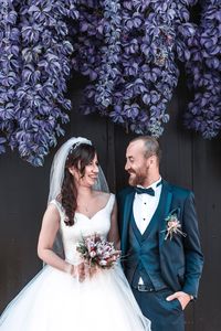 Smiling wedding couple looking each other face to face while standing against wall