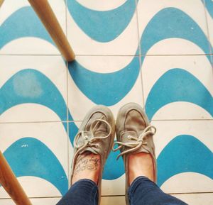 Low section of woman with tattoo wearing shoes over patterned tiled floor