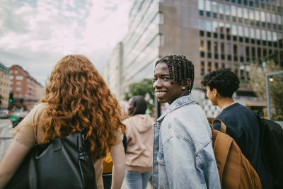 Portrait of happy braided hair teenage boy looking over shoulder while walking with friends in city street