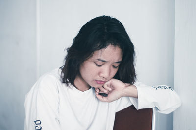 Sad young woman sitting against white wall