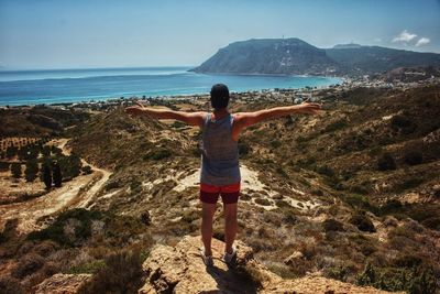 Rear view of man standing on cliff near sea