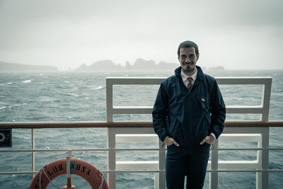 Portrait of man standing on railing against sea