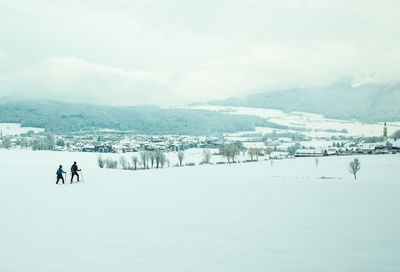 People skiing on snow covered landscape against sky