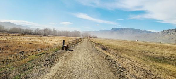 Empty road amidst field against sky